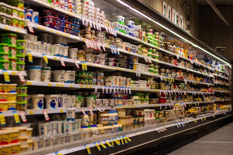 A supermarket dairy aisle with stacked yogurt cups and tubs along long refrigerated shelves.