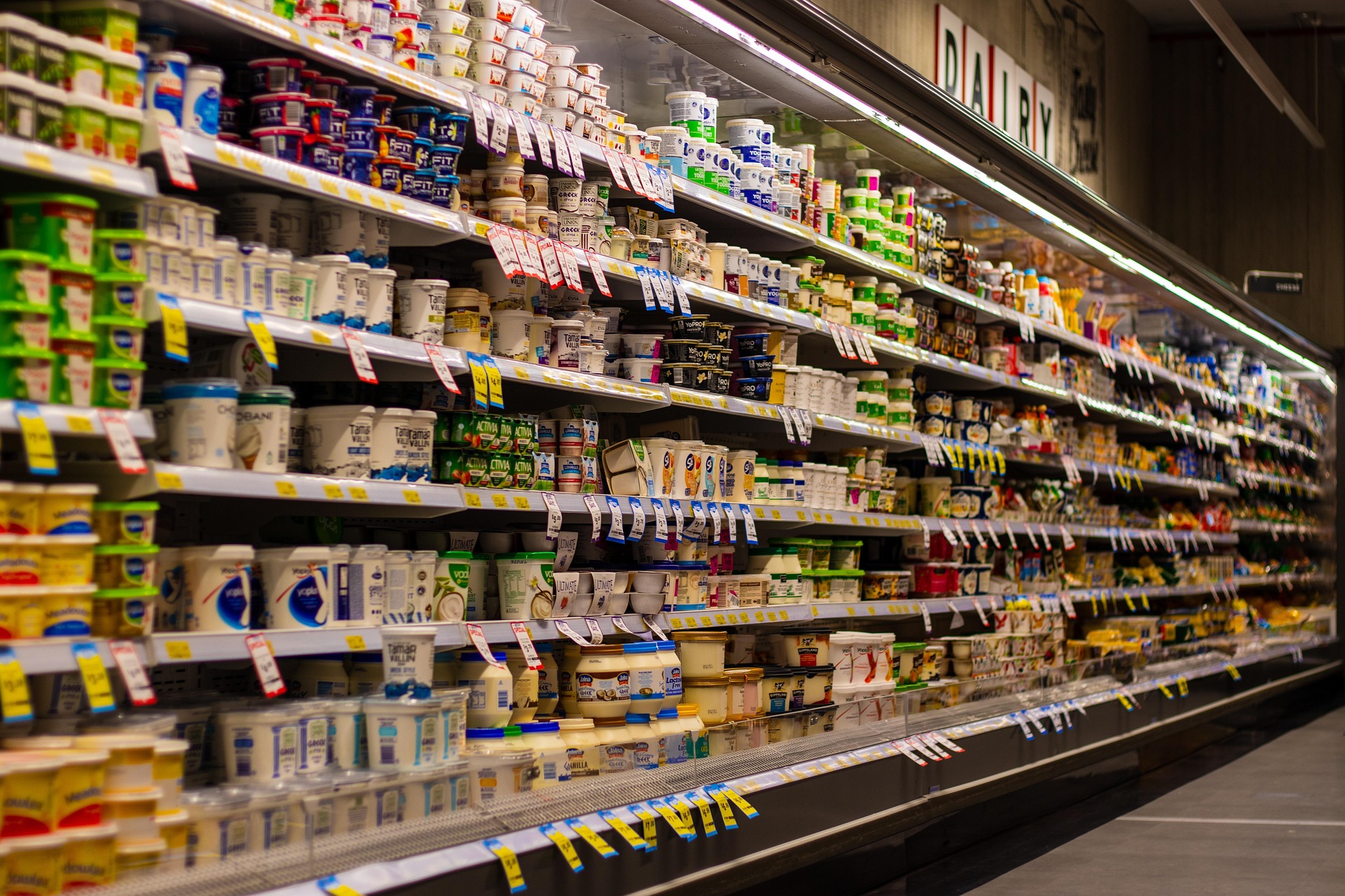 A supermarket dairy aisle with stacked yogurt cups and tubs along long refrigerated shelves.